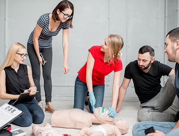 group of people practicing CPR techniques on a training mannequin with emphasis on learning proper emergency procedures and lifesaving skills through hands-on experience
