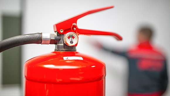 red fire extinguisher with gauge in focus background person demonstrating fire safety features related to fire safety training 2 safety tips 2 essential tools