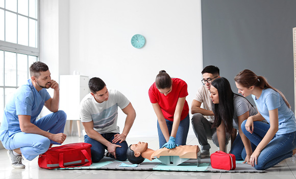 a group of people practicing CPR techniques on a training mannequin in a bright room first aid training session
