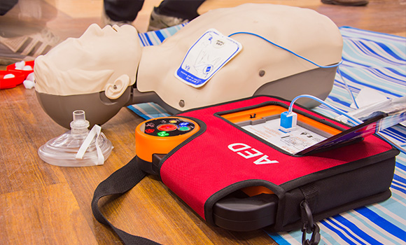 CPR training dummy with an AED device and mask on a blue striped surface promoting lifesaving skills and techniques for emergencies 2 life saving actions 2 equipment