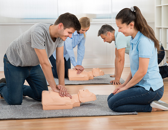 group performing CPR training on mannequins in a classroom setting demonstrating life saving skills and techniques to save lives 2 instructors 2 participants