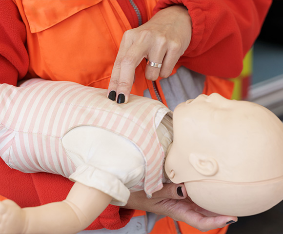 person performing CPR on baby doll during training session demonstrating lifesaving techniques for infant resuscitation 3 steps required