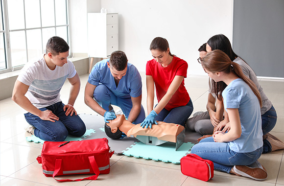 a group of people practicing CPR on a training mannequin in a classroom setting focused on emergency response skills sessions for 11 lifesaving techniques